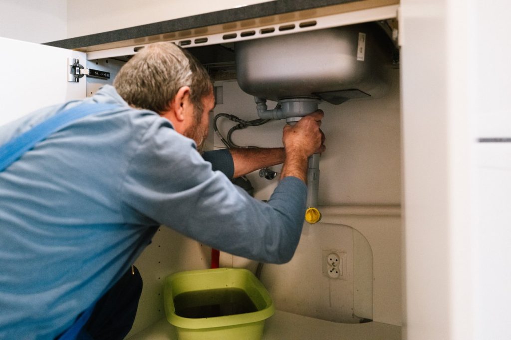 A plumber repairs a blocked drain in a kitchen 
